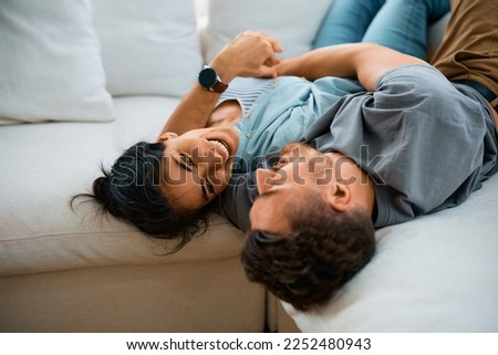 Happy couple talking while lying embraced on the sofa at home.