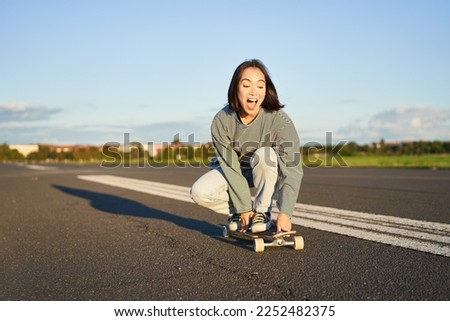 Portrait of carefree, happy asian girl skating, riding skateboard and laughing, enjoying sunny day.