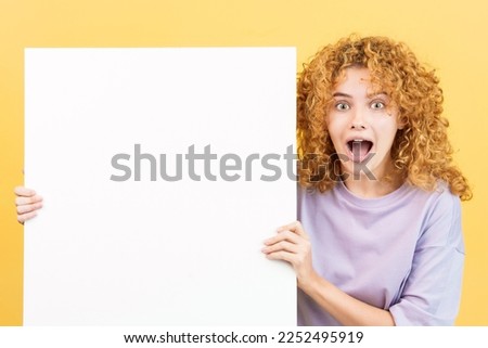 Surprised woman with curly hair holding a blank board