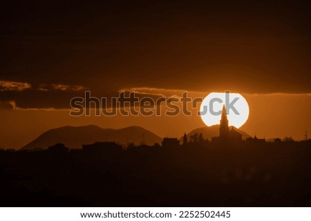 
giant sun behind church and mountains