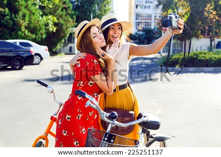Two best friends  posing near bright retro hipster bicycles and making self portrait on their vintage camera, making funny faces and having fun together, joy and happiness.