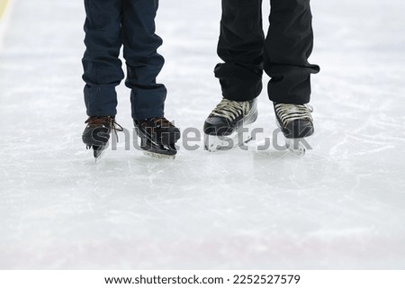 A child student and the teacher of ice skating during a lesson. View of their legs with ice skates trying to learn how to skate on ice.
