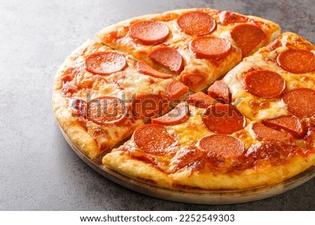 Classic pepperoni pizza with sausages, melted cheese and tomato sauce close-up on a wooden board on the table. horizontal
