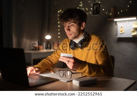 Student holding credit card typing numbers on computer keyboard while sitting at home or dormitory at the table. Online shopping concept. Copy space