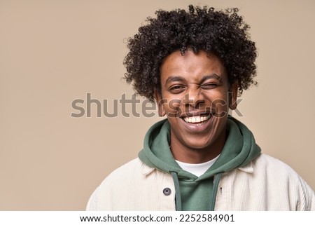 Happy young African American gen z guy winking isolated on beige background. Playful ethnic teen student, cool curly generation z teenager smiling with white perfect teeth, close up portrait. Royalty-Free Stock Photo #2252584901