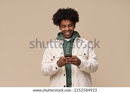 Young happy cool curly African American ethnic gen z guy holding cell phone, smiling teen using mobile digital apps on cellphone technology texting on smartphone isolated on light beige background.
