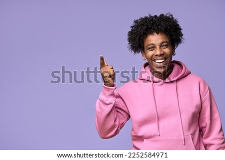 Happy African American teen guy pointing fingers up advertising new promo offer. Smiling ethnic student model showing presenting ads or having great idea standing isolated on light purple background. Royalty-Free Stock Photo #2252584971