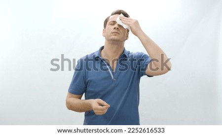 Young man complaining about summer heat isolated on white background. Angry man wiping sweat with napkin in hot weather. Stress, sweating, heat problem in summer weather. Royalty-Free Stock Photo #2252616533