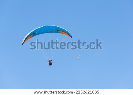 Two paraglider tandem fly against the blue sky, tandem paragliding on distance guided by a pilot