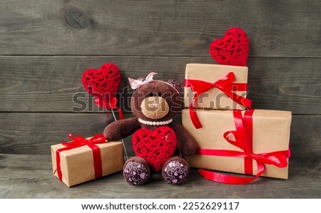On a wooden background, gifts for the holiday of Valentine's Day, a soft toy Teddy bear, red decorative hearts, boxes with gifts.  Decorative postcard, foreground, background picture.