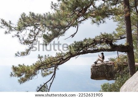 Young Asian woman sitting on a hill and enjoying the sea, sunset and mountains. and take pictures with beautiful views.
