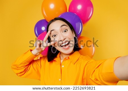 Close up happy fun young woman wear casual clothes celebrating near balloons do selfie shot pov on mobile cell phone show v-sign isolated on plain yellow background Birthday 8 14 holiday party concept
