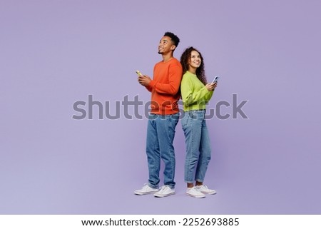 Full body side view young couple two friends family man woman of African American ethnicity wear casual clothes together hold use mobile cell phone look overhead isolated on plain purple background
