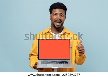 Young happy man of African American ethnicity 20s wear yellow shirt hold use work on laptop pc computer with blank screen workspace area show thumb up isolated on plain pastel light blue background