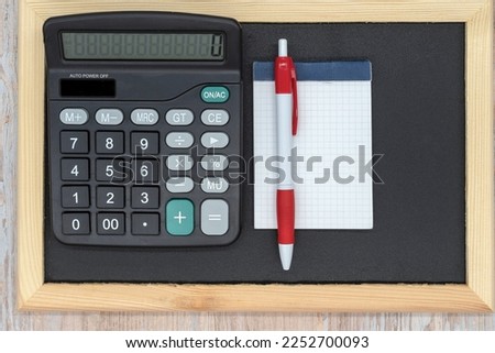 Black wooden blackboard, calculator, pen and electronic whiteboard. Top view. Copy space. Taxes, mathematics, investments, costs, payments.