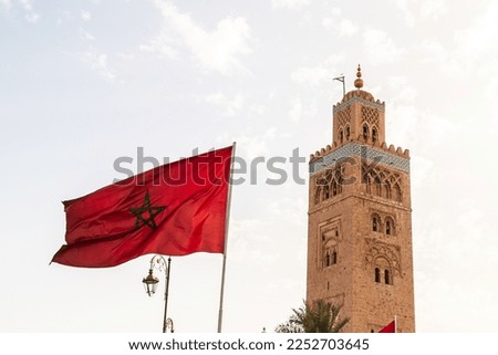 A closeup to the Koutoubia Mosque minaret in the Medina of Marrakesh in Morocco during the day. The Morocco flag can be seen in the foreground.