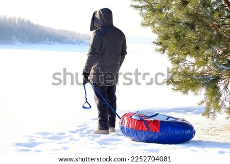 A adult man with a winter inflatable tube stands on the slope of a snowy mountain. An active lifestyle in the open air.