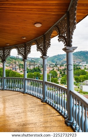 Carved wooden balcony with view to Rike park, hills and colorful buildings in historical Tbilisi, Georgia. Traditional decoration of Georgian house in Tiflis old town. Vertical orientation Royalty-Free Stock Photo #2252732923