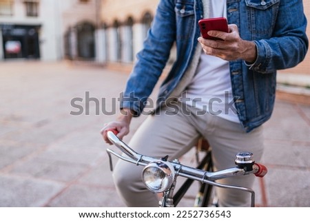 Cropped image of a young man in denim jacket consulting his cell phone on his vintage classic bicycle in the city.