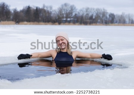 Winter swimming. Woman in frozen lake ice hole. Swimmers wellness in icy water. How to swim in cold water. Beautiful young female in zen meditation. Gray hat and gloves swimming clothes. Nature lake Royalty-Free Stock Photo #2252738221