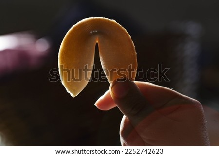 A child's hand holding a fortune cookie against a bright light, the golden color of the cookie contrasts with the hand of the child and the intense light creates a interesting effect.