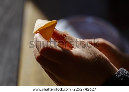 A child's hand holding a fortune cookie against a bright light, the golden color of the cookie contrasts with the hand of the child and the intense light creates a interesting effect.
