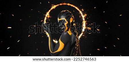 Woman on poster with gold face art. Yellow and black body paint. Young girl with bodypaint. An amazing model with makeup. Black background.