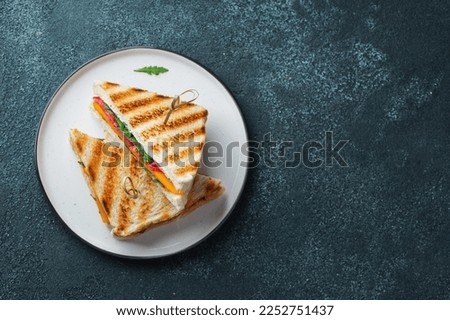 Two homemade sandwiches with sausage, cheese and arugula on a dark concrete background