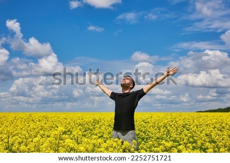 Attractive man with arms outstretched. Handsome young man standing in a field of blooming yellow rapeseed flowers. Royalty-Free Stock Photo #2252751721