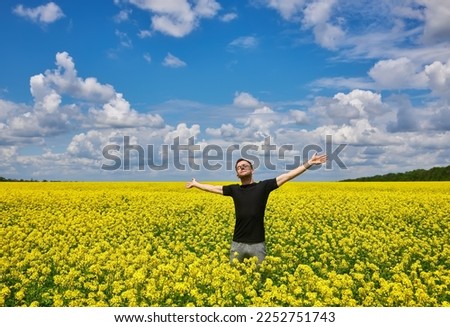Attractive man with arms outstretched. Handsome young man standing in a field of blooming yellow rapeseed flowers. Royalty-Free Stock Photo #2252751743