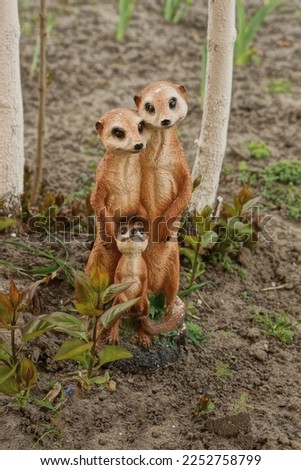 decorative ceramic sculpture toy of three brown gophers stands on gray ground in a summer garden among green vegetation