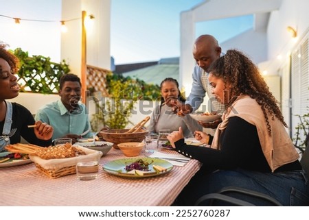 Happy african family doing dinner while eating healthy food at home patio - Lifestyle home moments and summer concept - Main focus on right girl hand