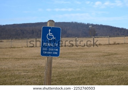 A blue handicap parking sign that reads "Penalty," with fines in US dollars.