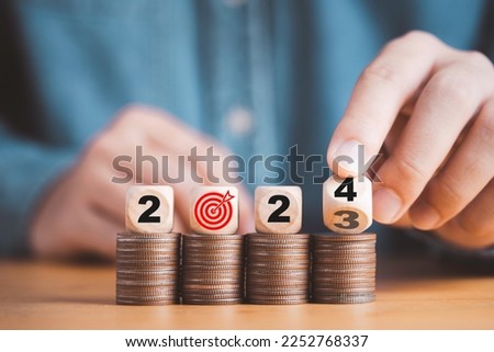 Businessman hand flipping wooden block cube from 2023 to 2024 on coins stacking for setup objective target business cost and budget planing of new year concept. Royalty-Free Stock Photo #2252768337