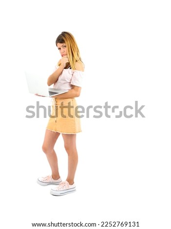 Young teenager woman thinking while holding a laptop with her hand against a white background