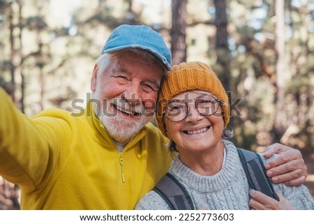 Head shot portrait close up of cute couple of old seniors taking a selfie together in the mountain forest looking at the camera smiling having fun enjoying. Two mature people hiking.