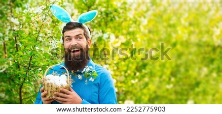 Funny man in rabbit costume hold easter eggs. Bearded man holding basket of Easter eggs. Horizontal photo banner for website header design.