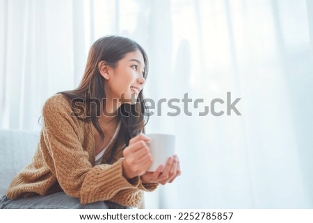 Happy asian woman relaxing drinking hot coffee or tea in holiday morning vacation on armchair at home, Cosy scene, Smiling pretty woman drinking hot tea in autumn winter. copy space. Royalty-Free Stock Photo #2252785857