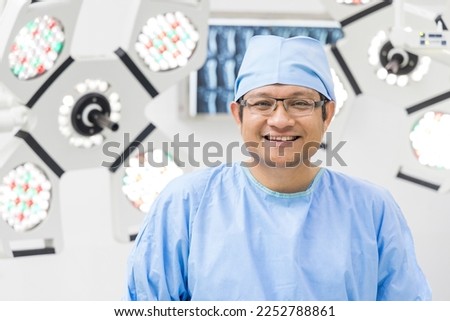 Surgeon smiling in blue surgical gown suit inside modern operating room with surgical mask. Doctor wear gloves prepare for surgery in private clinic. Medical concept.