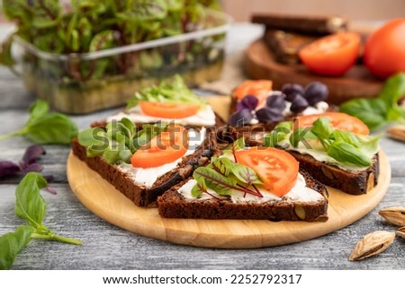Grain rye bread sandwiches with cream cheese, tomatoes and sorrel microgreen on gray wooden background and linen textile. side view, close up, selective focus. Royalty-Free Stock Photo #2252792317