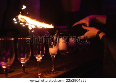 Closeup girl bartender pours champagne into glasses. Rest in a nightclub, pub, restaurant. Decorative firework sparkling column of fire on a bottle of champagne Royalty-Free Stock Photo #2252804583