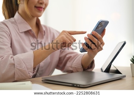 Cropped shot of smiling asian woman employee sitting at office desk and using smart phone.