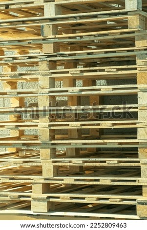 Stack of raw construction or industrial warehouse pallets used to transport goods and stack comercial products. In shade near back of building made of recycled wood and nailed together.