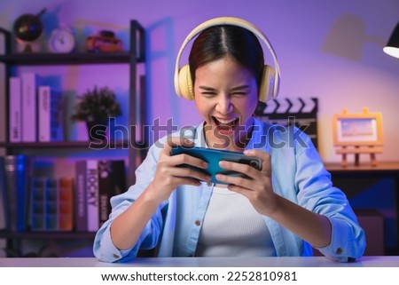 Excited Young Asian woman wearing headset and playing online game on smartphone with live broadcasting on internet. Royalty-Free Stock Photo #2252810981