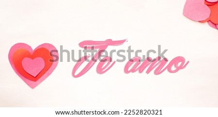 Image of pink colored hearts cut out on a white background with the phrase I love you in Spanish