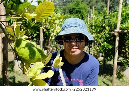 An Asian woman taking a picture with a large lemon in a lemon farm.