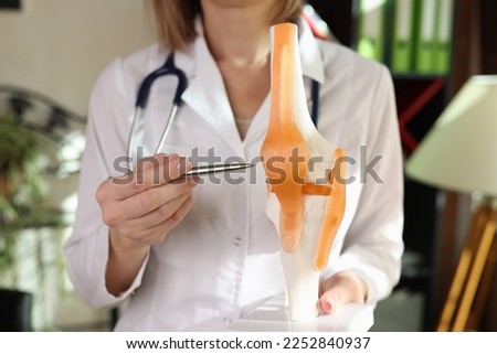 Woman doctor holds anatomical model of human knee-joint and points by pen. Knee and meniscus disease, sickness prevention and orthopedic concept. Royalty-Free Stock Photo #2252840937
