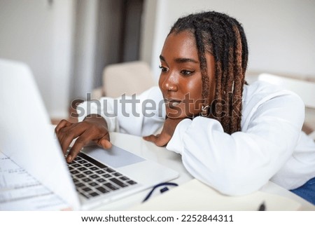 Remote job, technology and people concept - young African business woman with laptop computer and papers working at home office during the Covid-19 health crisis.