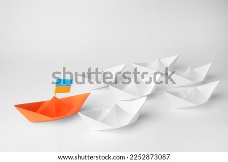 Group of paper boats following orange one on white background. Leadership concept