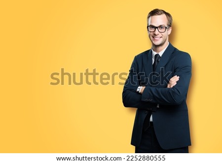 Portrait of businessman in eye glasses, spectacles, black suit and tie, with crossed arms, on vivid yellow background. Business concept. Smiling man at studio picture. Copy space for ad.